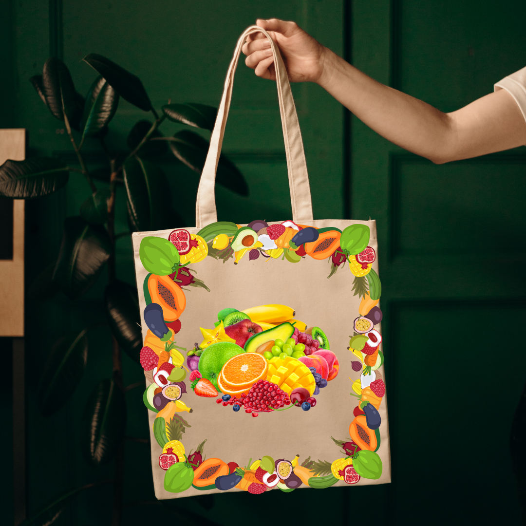 A beige canvas tote bag with a colorful fruit print, held by a person's hand against a dark green background with a plant.